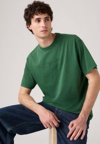 Zelené bavlněné tričko s kulatým výstřihem a krátkými rukávy. Má embosované logo na přední straně a volný střih.