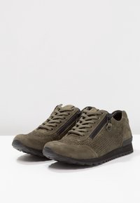Sneakers in suede verde oliva con accenti perforati, cerniere in metallo nero e suole in gomma testurizzata per la presa. Design classico con lacci.