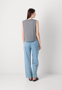 Ermeløs marineblå mønstrete topp kombinert med lyseblå rette jeans. Toppens geometriske design gir en avslappet passform. Svart sandaler er brukt.