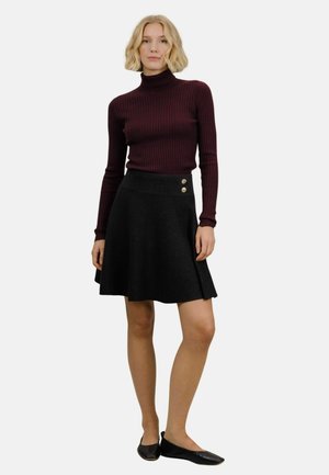 Burgunderfarget ribbete turtleneck-genser kombinert med et svart utsvingt skjørt med to gullknapper i midjen. Svart flate sko fullfører antrekket.