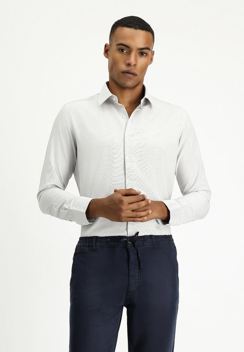 Camisa de manga larga gris claro con un sutil patrón texturizado, cuello abotonado y puños ajustados, combinada con pantalones de chándal navy con cordón.