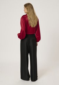 Red satin blouse with puffed sleeves and high neck, paired with high-waisted, black wide-leg trousers. Smooth texture and elegant fit.