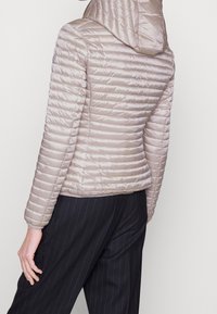 Lichtbeige pufferjack met horizontaal gestikt patroon, een capuchon en elastische manchetten, gecombineerd met zwarte gestreepte broek.