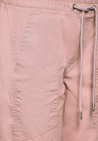 Light pink shorts made of smooth fabric, featuring an elastic waist with a drawstring, side pockets, and subtle stitching details.