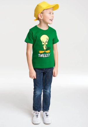 Green cotton t-shirt featuring a cartoon Tweety graphic, paired with dark blue jeans and white sneakers. The child wears a bright yellow cap.