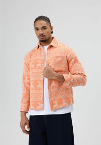 Oranje geruit flanellen overhemd met hertenmotieven, voorzien van een knoopsluiting aan de voorkant, kraag en lange mouwen, gemaakt van een gestructureerde stof.