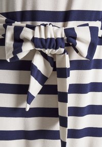 Pruhovaná látka v námořnické modré a bílé barvě má velkou mašli uvázanou v pase, s měkkou texturou a neformálním designem.