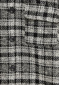 Tissu à motif pied-de-poule noir et blanc avec trois boutons noirs et une poche à rabat sur un vêtement texturé.