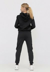 Haut à capuche noir avec des accents blancs et une poche kangourou, associé à un jogging noir cargo avec des poches latérales et des poignets élastiques. Baskets blanches.