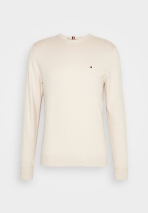 Pull crème à manches longues en tissu doux, avec un col rond et un petit logo rouge et bleu sur la poitrine.