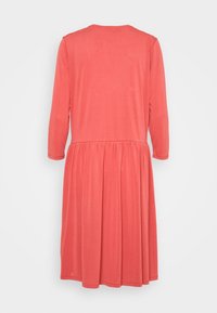 Korallfärgad långärmad klänning med rund halsringning, rynkad midja och flödande kjol, tillverkad av ett mjukt tyg.