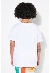 Hvid bomulds t-shirt med en afslappet pasform, korte ærmer og en rund halsudskæring. Viser en synlig tatovering på bagsiden af nakken.