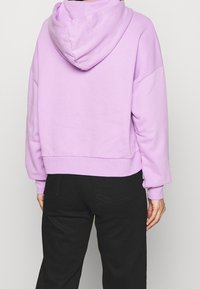 Hoodie cropped di un leggero colore viola con cappuccio, dotato di spalle cadenti e polsini a coste. Tessuto morbido in misto cotone, design semplice.