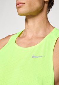 Neonowy zielony bezrękawnik sportowy wykonany z oddychającego materiału, z teksturowanym wzorem i srebrnym logo Nike umieszczonym na klatce piersiowej.