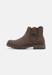 Bottine Chelsea en cuir marron avec des panneaux élastiques sur les côtés et une languette, dotée d'une semelle texturée et d'un branding subtil sur le côté.