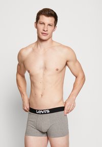 Harmaat puuvillaiset boxerit, joissa on musta vyötärönauha, jossa on Levi's-logo. Malli on ilman paitaa, mikä korostaa shortsien istuvuutta ja leikkausta.