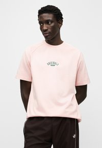 Ροζ ανοιχτό ροζ κοντομάνικο μπλουζάκι με στρογγυλή λαιμόκοψη. Διαθέτει πράσινο λογότυπο "Originals" στο κέντρο και τις εμβληματικές τρεις ρίγες στα μανίκια.