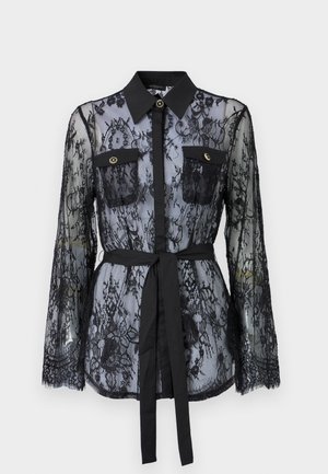 Blouse en dentelle noire avec des manches longues, des poches poitrine boutonnées, un col classique et une ceinture en tissu nouée à la taille. Design transparent.