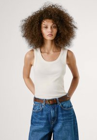 Canotta bianca con scollo a barchetta, abbinata a pantaloni di jeans blu e una cintura marrone con una fibbia decorativa. Tessuto liscio, stile casual.