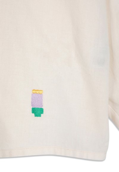Petite broderie abstraite avec des formes jaunes, violettes et vertes sur le bas d'un vêtement en tissu beige.