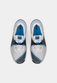 Pair of white and blue athletic shoes with black accents, blue insoles, and labeled lace tuck system, viewed from above on a white background.