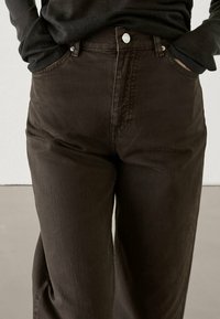 Bruna denimbyxor med hög midja, med knappstängning och framfickor. Tyget har en slät yta och rak bendesign.