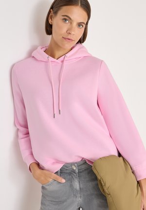 Roze hoodie met trekkoorden, zachte textuur, relaxed fit. Gepaard met grijze jeans en een groene pufferjack.