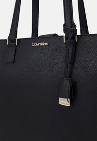 Czarna torebka wykonana z ziarnistej skóry ze złotymi elementami. Posiada podwójne uchwyty oraz metkę z logo Calvin Klein.