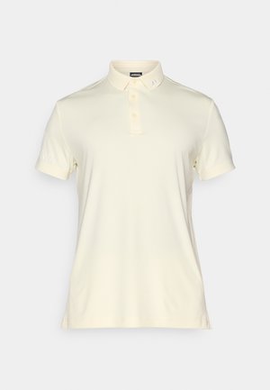 Polo krekls gaiši krēmkrāsā, īsām piedurknēm, ar trīs pogu aizdari, diskretā logo detaļa uz apkakles un gluda auduma tekstūra.