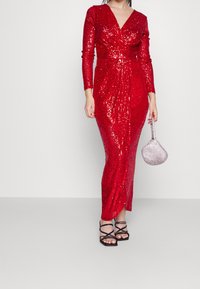 Rotes, mit Pailletten besetztes Kleid mit langen Ärmeln und tiefem V-Ausschnitt. Hat eine figurbetonte Silhouette und einen Oberschenkel hohen Schlitz. Kombiniert mit schwarzen Sandalen mit Riemchen und einer silbernen Handtasche.