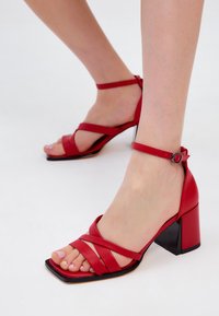 Rode leren sandalen met blokhak, crisscross banden en een enkelbandje, met een vierkante neus en een glanzende zwarte hak.