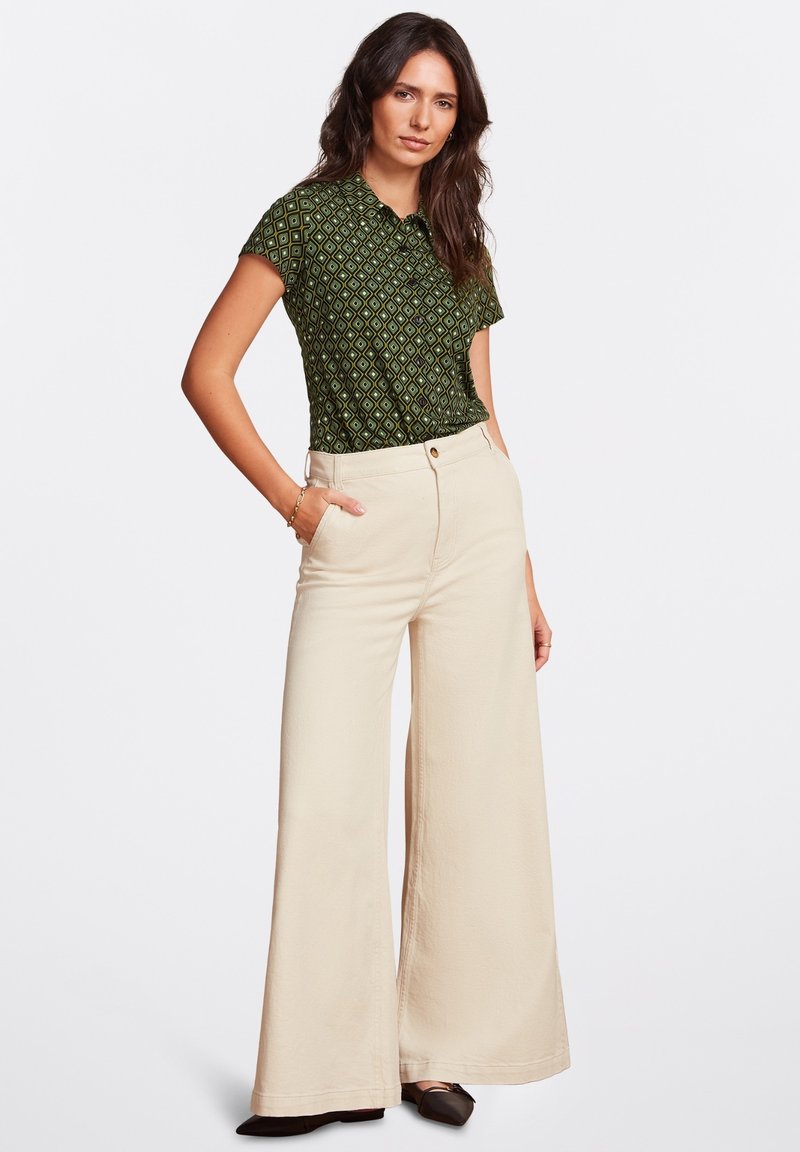 Polo shirt verde a righe con colletto abbinato a pantaloni beige a vita alta e a gamba larga. Tessuto liscio, delicato motivo a diamante e tasche.