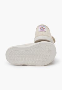 Beige plátěné boty s bílou gumovou podrážkou. Podpatky mají barevnou nášivku s opicí. Texturovaný vzor podrážky.