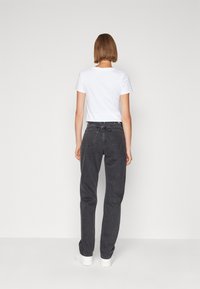 Jeans negros de tiro alto con un ajuste relajado, con dos bolsillos traseros y un diseño minimalista, combinados con una camiseta blanca de manga corta.