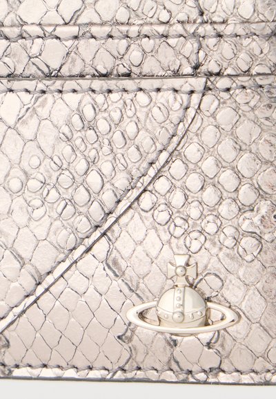 Κοντινή λήψη επιφάνειας από δέρμα με μεταλλική ασημί υφή φιδιού, με ένα μικρό λευκό έμβλημα σε σχήμα σφαίρας και σταυρού.