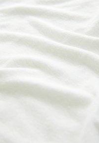 White cotton fabric with a soft, smooth texture, displaying subtle wrinkles and folds, creating a wave-like appearance.