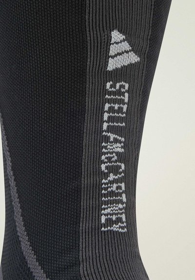Black knitted sock with grey accents and textured fabric, featuring a logo printed in white on the side.