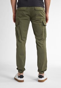 Olivenfarvede cargo bukser med sidelommer, elastiske manchetter og et let væv; parret med hvide sneakers med sorte detaljer.