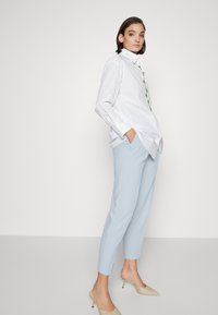 White shirt with a flower-embroidered collar, paired with light blue trousers and beige heels. The shirt has a relaxed fit and long sleeves.