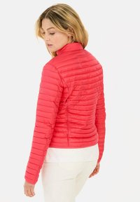 Rote gepolsterte Jacke mit horizontaler Steppung, hohem Kragen, tailliertem Schnitt und glatter Textur. Getragen über einem weißen Hemd, von hinten präsentiert.
