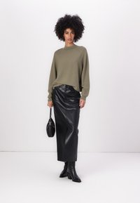 Olive green knit sweater with a high neckline, paired with a black leather midi skirt. Accessories include a small black handbag and black heeled boots.