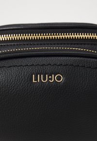 Borsa in pelle nera testurizzata con zip dorata e logo LIU•JO in lettering dorato impresso sulla parte anteriore.