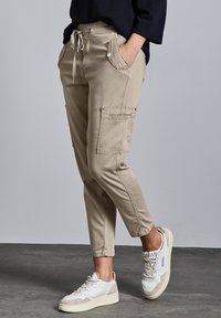 Beige cargobroek met een elastische tailleband, zijzakken en opgerolde enkels, gecombineerd met witte sneakers met beige accenten.