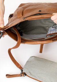 Bruine leren tas met een gestreepte stoffen binnenkant en een kleinere gestreepte pouch. De banden hebben contrasterende rode stiksels en metalen hardware.