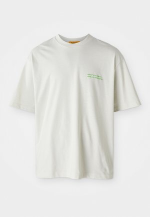 Witte katoenen t-shirt met een relaxte pasvorm, voorzien van groene tekst geborduurd op de borst die zegt: "Werk hard, feest harder."
