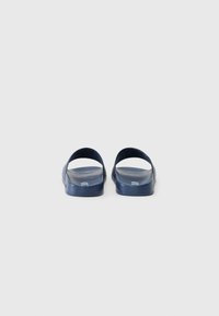Navy blue kumisaappaat, joissa on avoimet takuosat, sileä pinta ja minimalistinen muotoilu. Kummassakin kumisaappaassa on kaksi rinnakkaista valkoista yksityiskohtaa.