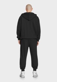 Czarna bluza z kapturem i dresy, wykonane z miękkiego materiału, z luźnym krojem, dużym kapturem i elastycznymi mankietami, w połączeniu z białymi trampkami.