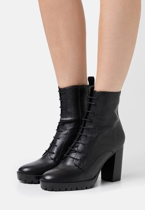 Sorte ankelstøvler i læder med snørebånd, en sidelås og en kraftig høj hæl. Har en tekstureret overflade og rillede såler.
