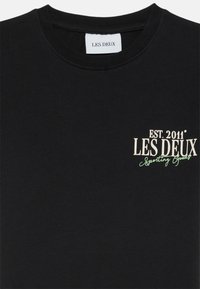 Schwarzes Baumwoll-T-Shirt mit Rundhalsausschnitt. Mit bedrucktem Text in Weiß und Grün: "EST. 2011 LES DEUX Sporting Goods." Kurzärmelig.