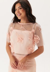 Top floreale rosa trasparente con maniche corte, caratterizzato da fiori ricamati, un collo delicato e una texture liscia. Abbinato a una gonna coordinata.